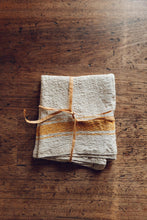 Load image into Gallery viewer, A natural linen kitchen towel with yellow striped borders, tied with natural fibre, on antique timbers at Settle Norfolk, UK | Copyright Settle Norfolk, UK