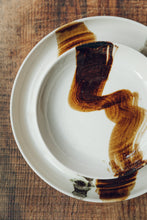 Load image into Gallery viewer, Settle | By Noo Ceramics Brushstroke Open Bowl - close view of a pale handmade ceramic bowl with a generous base and gently curved sides, hand decorated with a thick brush stroke of chocolate brown across the bowl's interior. Set on antique interior timbers at Settle.