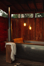 Load image into Gallery viewer, SETTLE | Pico Goods Bath Towel - a handwoven organic cotton bath towel in a natural off-white with tasselled edging is draped on a wooden bath table next to the private wood-fired outside bath at Settle's Cabin retreat .