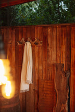 Load image into Gallery viewer, SETTLE | Pico Goods Bath Towel - a handwoven organic cotton bath towel in a natural off-white with tasselled edging is hung on a wall peg in the privacy of the wood-fired bathroom at Settle's Cabin retreat .