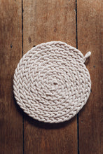 Load image into Gallery viewer, Shop at Settle The Chemists Daughter - overview of a lovely, circle woven trivet handmade from 100% recycled pale cotton, set on antique timbers