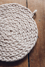 Load image into Gallery viewer, Shop at Settle The Chemists Daughter - close-up of a lovely, circle woven trivet handmade from 100% recycled pale cotton, set on antique timbers
