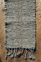 Load image into Gallery viewer, Shop with Settle | Cabin Woven - handwoven table runner, made from handspun wool, with tasselled ends and a subtle fawn brown on charcoal stripe, displayed on antique timbers at Settle. 