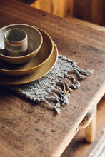 Load image into Gallery viewer, Shop with SETTLE | Cabin Woven - a place setting of handmade ceramics is set on a handwoven table runner made from handspun wool, with tasselled ends and subtle brown on charcoal stripe, on an antique timber table at Settle. 