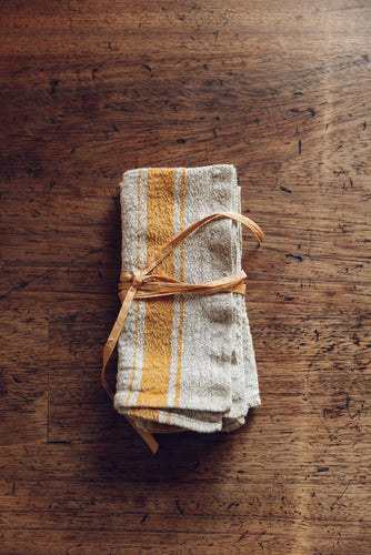 A pair of 2 natural linen napkins with yellow striped borders, tied with natural fibre, on antique timbers at Settle Norfolk, UK | Copyright Settle Norfolk, UK