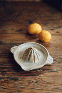 SETTLE | Every Story Ceramics Citrus Juicer - foreground of a ceramic citrus juicer handmade in natural speckled clay with two lemons behind it, set on antique timbers at Settle.