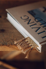 Load image into Gallery viewer, Shop with Settle | Cabin Woven - charming detail of tasselled end of handwoven bookmark marking a place in a closed hardback lifestyle book.