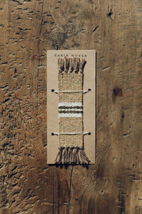 Shop with Settle | Cabin Woven - handwoven from handspun wool bookmark with tasselled ends and central stripe detail; fawn brown with white and charcoal stripe. 