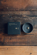 Load image into Gallery viewer, Settle | Ume ~ overview of an elegant black stoneware bowl containing a small gold-coloured incense dome, next to a square black box with Ume&#39;s motif and name in gold, all set on antique timbers in one of Settle&#39;s luxury retreats. 