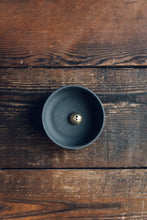 Load image into Gallery viewer, Settle | Ume ~ closer view of an elegant black stoneware bowl containing a small gold-coloured incense dome set on antique timbers in one of Settle&#39;s luxury retreats.