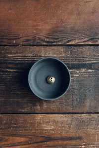 Settle | Ume ~ closer view of an elegant black stoneware bowl containing a small gold-coloured incense dome set on antique timbers in one of Settle's luxury retreats.