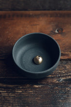 Load image into Gallery viewer, Settle | Ume ~ closer diagonal view of an elegant black stoneware bowl containing a small gold-coloured incense dome, next to a square black box with Ume&#39;s motif and name in gold, all set on antique timbers in one of Settle&#39;s luxury retreats.