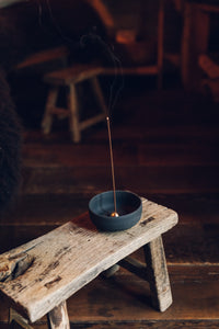 Settle | Ume ~ further view of an elegant black stoneware bowl containing a small gold-coloured incense dome which holds a lighted incense stick, sitting on an antique trestle in one of Settle's luxury retreats.
