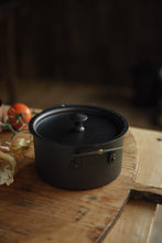 Load image into Gallery viewer, Settle | Netherton Foundry - close view of a black spun iron stock pot, with lid, set on an antique wooden chopping board in the heritage kitchen of one of Settle&#39;s luxury retreats.  