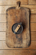 Load image into Gallery viewer, Shop at Settle | Netherton Foundry - cast iron charcoal grey glamping pot and lid, with wooden handle removed and fixed across the lid, set on a handsome antique wooden board.