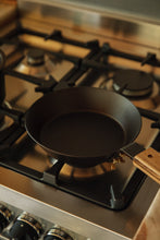 Load image into Gallery viewer, Shop with Settle | Netherton Foundry - overview of a hand-spun cast iron pan with wooden handle in use on a gas hob.