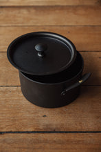 Load image into Gallery viewer, Settle | Netherton Foundry - closer view of a black spun iron stock pot and its lid set on antique wooden timbers.