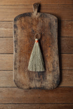 Load image into Gallery viewer, SETTLE | Wild Crafted Home Primitive Handmade Brush - a triangular shaped handmade brush with pale gold fibres and a stem made of wound amber-coloured fibres with a looped leather band, placed on a large antique chopping board on antique timbers at Settle.