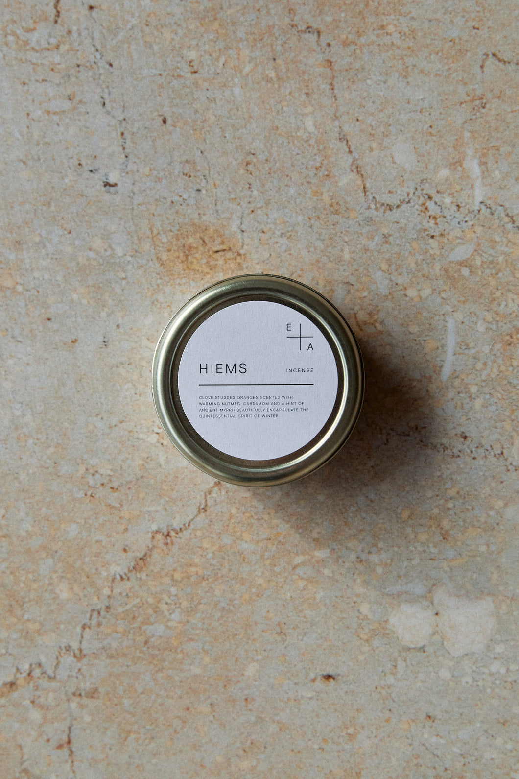 Shop with Settle | Essence + Alchemy Hiems Incense Cones - overview of a gleaming tin labelled HIEMS Essence + Alchemy containing scented incense cones, set on a pale grey marble surface against an apricot marble background at Settle.  