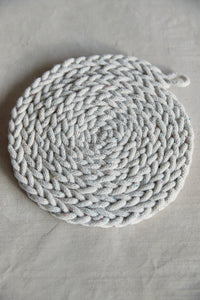 Shop at Settle The Chemists Daughter - close-up of a lovely, circle woven trivet handmade from 100% recycled pale cotton, set against a pale background