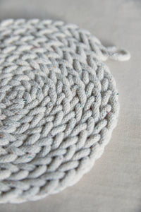Shop at Settle The Chemists Daughter - close-up of a lovely, circle woven trivet handmade from 100% recycled pale cotton, set against a pale background  