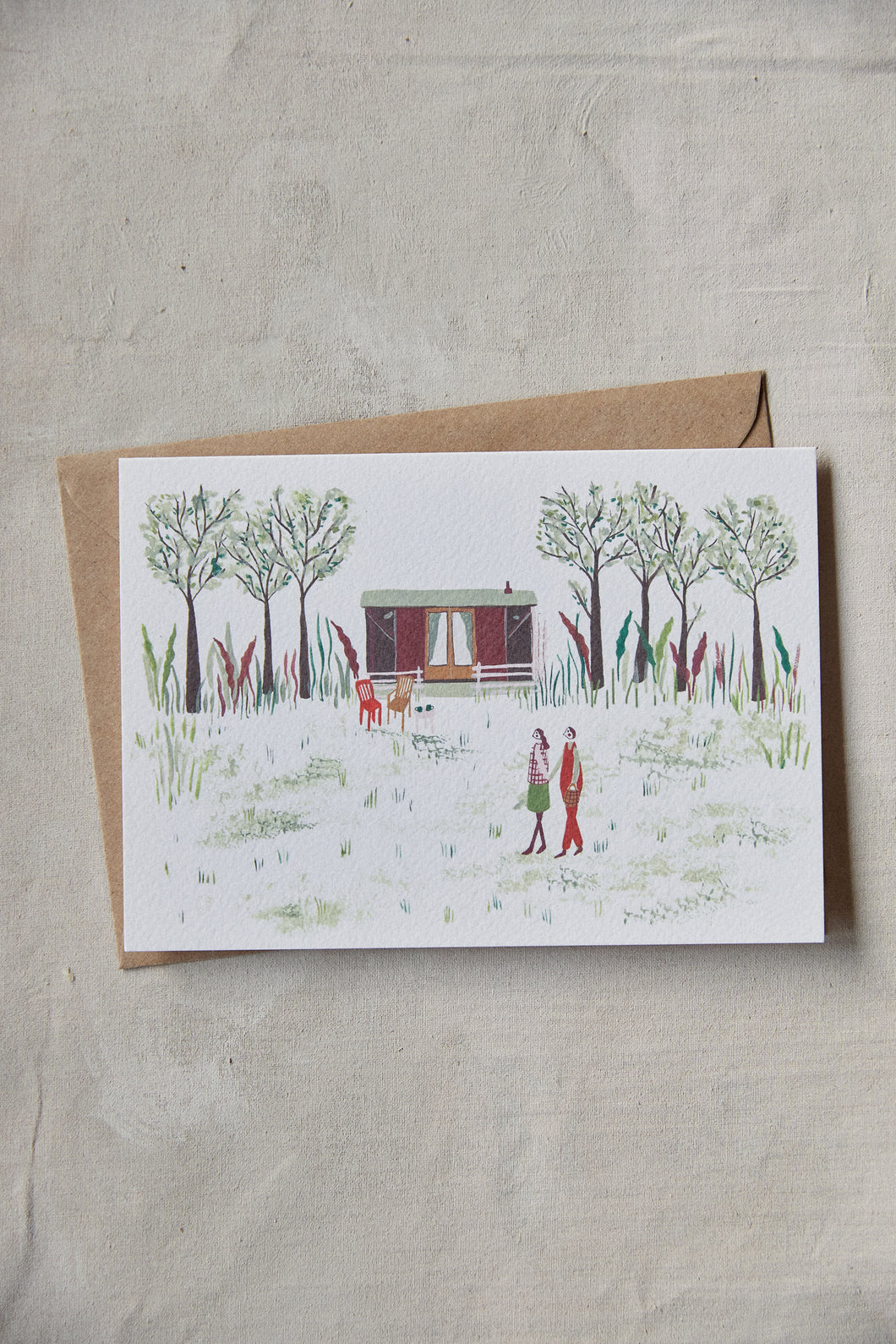 Shop at Settle | Harriet Watson A Walk in the Woods - charming hand illustrated colour greetings card of two guests enjoying a walk in Settle's wooded park, with Carriage No. 2 nestled in the background, set against a pale timber surface.