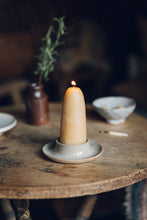 Load image into Gallery viewer, SETTLE - a gently lit chunky candle made from golden beeswax sits comfortably on an artisan ceramic candleholder, on an antique timber table in one of Settle&#39;s luxury retreats.  