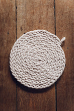 Load image into Gallery viewer, Shop at Settle The Chemists Daughter - overview of a lovely, circle woven trivet handmade from 100% recycled pale cotton, set on antique timbers  