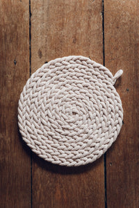Shop at Settle The Chemists Daughter - overview of a lovely, circle woven trivet handmade from 100% recycled pale cotton, set on antique timbers  