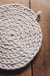 Shop at Settle The Chemists Daughter - close-up of a lovely, circle woven trivet handmade from 100% recycled pale cotton, set on antique timbers  