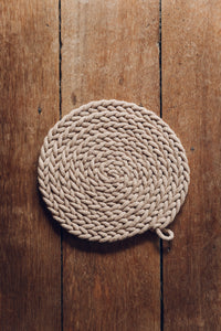 Shop at Settle The Chemists Daughter - overview of a lovely, circle woven trivet handmade from 100% recycled pale cotton, set against antique timbers  