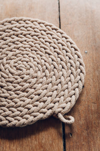 Shop at Settle The Chemists Daughter - close-up of a lovely, circle woven trivet handmade from 100% recycled pale cotton, set on antique timbers  