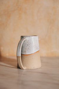 SETTLE | Every Story Ceramics Cosy Mug - closeup on the elegant long handle of a sturdy handmade ceramic mug made in pale speckled clay with unique markings. Its base is broader than its rim and the elegant long handle curves from the top rim to the base making this mug hard to knock over. Pictured on a grey marble surface with a pale background at Settle. 