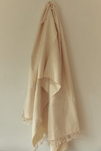 Load image into Gallery viewer, SETTLE | Pico Goods Bath Towel - a handwoven organic cotton bath towel in a natural off-white with tasselled edging is hung on a wall peg at Settle.