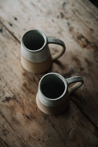 SETTLE | Every Story Ceramics Cosy Mug - top view of two handmade ceramic mugs handmade in pale speckled clay. With their broad bases and long curved handles these mugs are sturdy and practical, seen here on antique timbers at Settle.